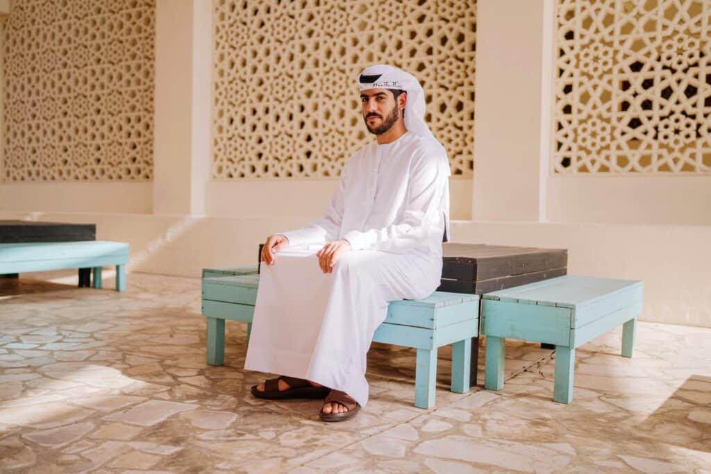 Arabic man wearing traditional clothing dishdasha sitting on a traditional bench